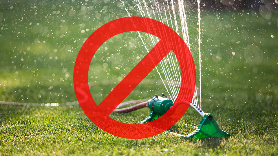 Förbudssymbol över en vattenspridare som står påslagen på gräsmatta.