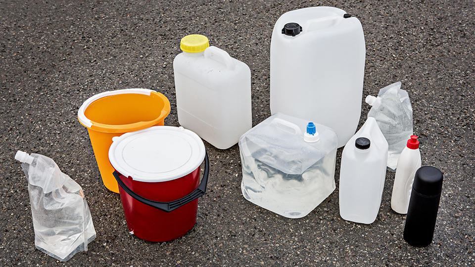Flera olika typer av behållare för vatten står på marken, till exempel dunkar, spann, påsar, flaskor.