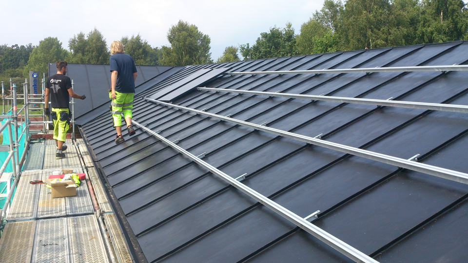 Två personer installerar solceller på ett tak.